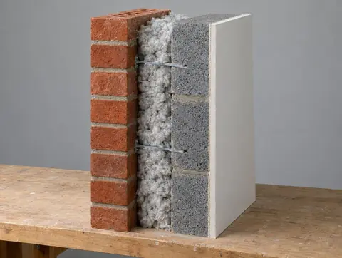 Cutaway sample of a cavity wall: red brick outer leaf, cavity filled with blown mineral wool, concrete block inner leaf